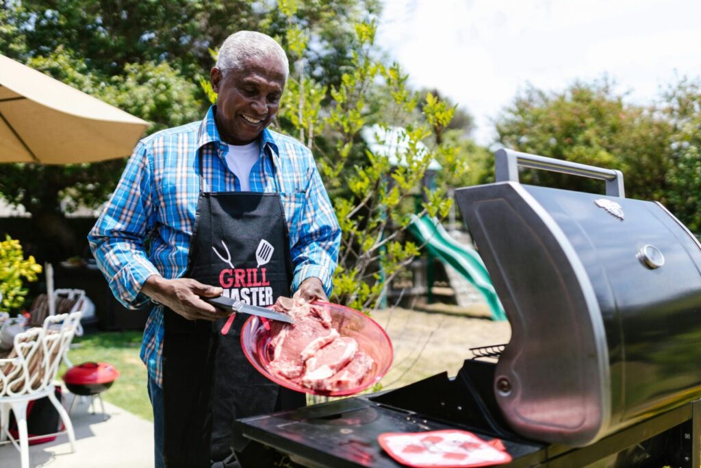 Smiling man grilling steaks outside on a sunny day, enjoying summer barbecue.