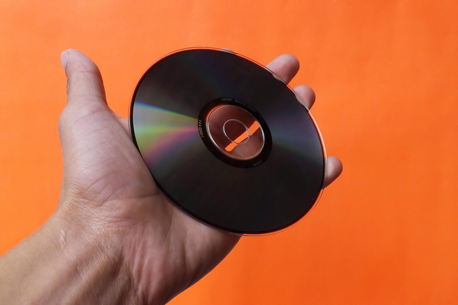 Close-up of a hand holding a classic compact disc with an orange background, evoking nostalgia.